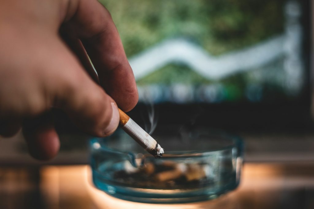 person holding cigarette stick and round glass ashtray