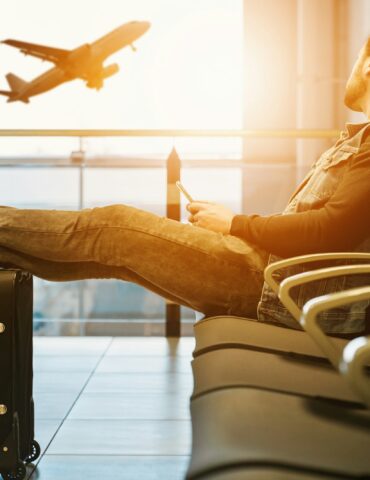 man sitting on gang chair with feet on luggage looking at airplane
